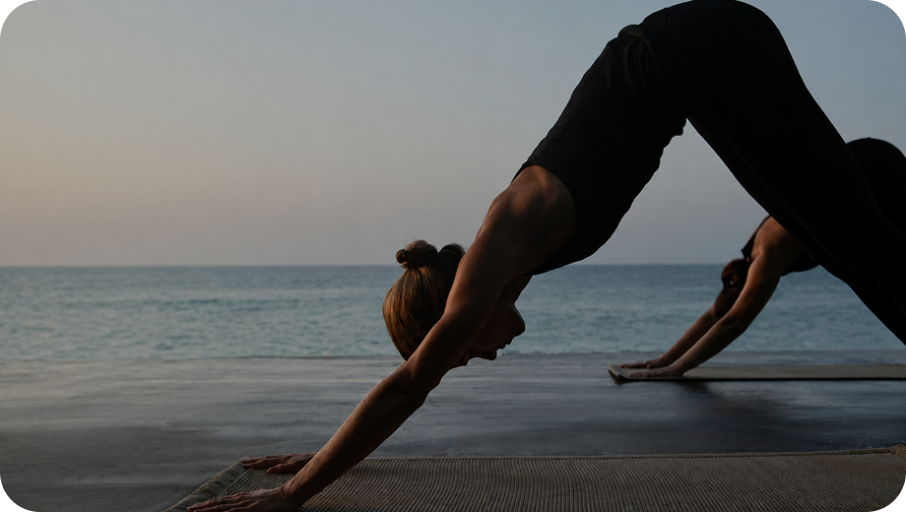 Woman in a downward-dog yoga pose on a beach at dawn